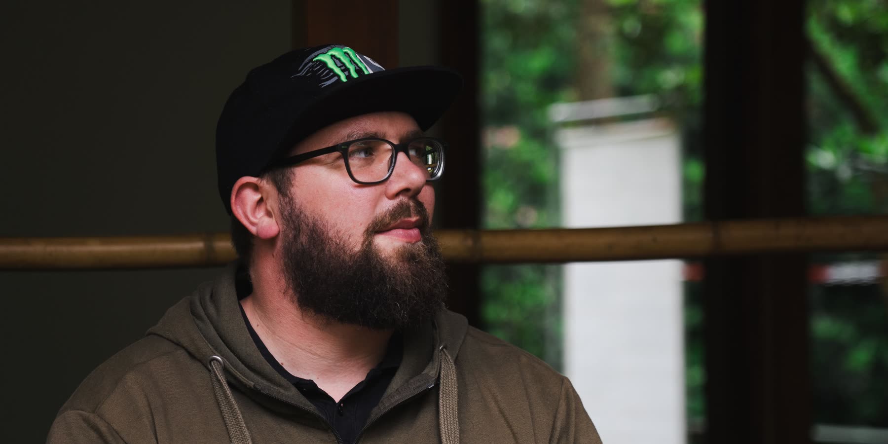 Wouter van Marrum, seated by a window in a green hoodie and a black cap, looking off to one side.